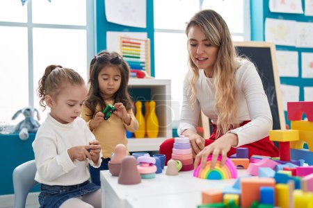 Photo for Teacher with girls playing with geometry blocks sitting on table at kindergarten - Royalty Free Image