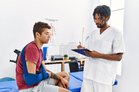 Foto de Dos hombres fisioterapeuta y paciente que tienen sesión de rehabilitación escribiendo informe de accidente en la clínica - Imagen libre de derechos