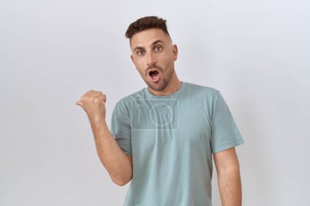 Photo for Hispanic man with beard standing over white background surprised pointing with hand finger to the side, open mouth amazed expression. - Royalty Free Image