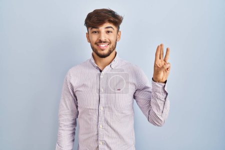 Photo for Arab man with beard standing over blue background showing and pointing up with fingers number three while smiling confident and happy. - Royalty Free Image
