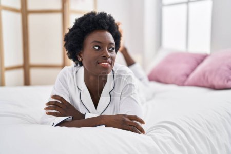 Téléchargez les photos : Jeune femme afro-américaine souriante confiante couchée sur le lit dans la chambre - en image libre de droit