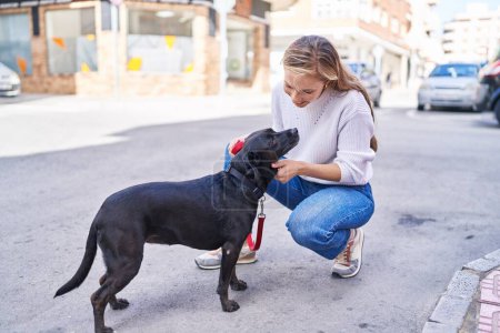Photo for Young blonde woman smiling confident touching dog at street - Royalty Free Image