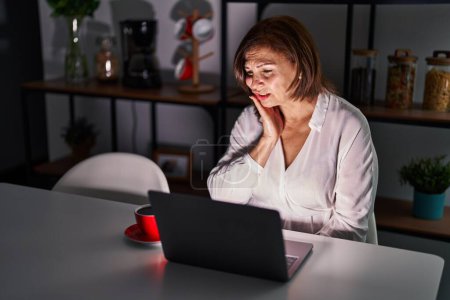 Photo for Middle age hispanic woman using laptop at home at night touching mouth with hand with painful expression because of toothache or dental illness on teeth. dentist - Royalty Free Image