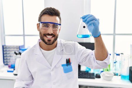 Téléchargez les photos : Jeune homme hispanique portant l'uniforme scientifique tenant le tube à essai au laboratoire - en image libre de droit