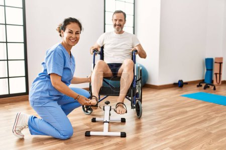 Foto de Hombre y mujer de mediana edad que tienen sesión de rehabilitación pedaleando sentados en silla de ruedas en la clínica de fisioterapia - Imagen libre de derechos