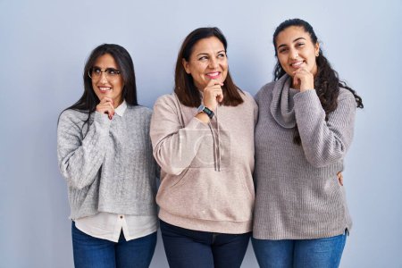 Photo for Mother and two daughters standing over blue background with hand on chin thinking about question, pensive expression. smiling and thoughtful face. doubt concept. - Royalty Free Image