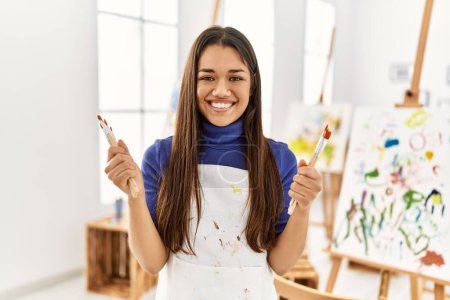 Photo for Young latin woman smiling confident holding paintbrushes at art studio - Royalty Free Image
