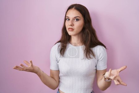 Photo for Young hispanic girl standing over pink background clueless and confused with open arms, no idea concept. - Royalty Free Image