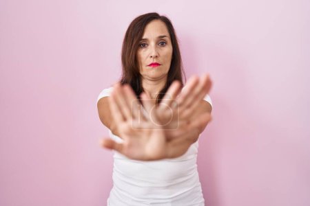 Téléchargez les photos : Moyen âge brunette femme debout sur fond rose expression de rejet croisement des bras et des paumes faisant signe négatif, visage en colère - en image libre de droit