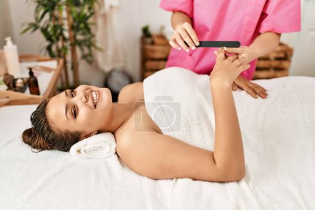 Photo for Young beautiful hispanic woman lying on table having manicure treatment at beauty salon - Royalty Free Image