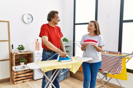Foto de Mediana edad hombre y mujer pareja sonriendo confiado planchar ropa en la lavandería - Imagen libre de derechos