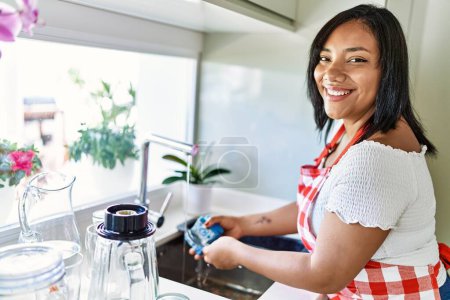 Téléchargez les photos : Hispanique brune femme lave la vaisselle à la cuisine - en image libre de droit