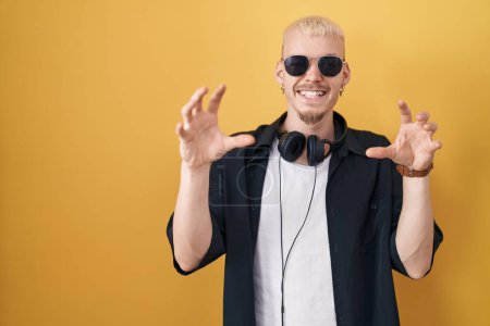 Photo for Young caucasian man wearing sunglasses standing over yellow background smiling funny doing claw gesture as cat, aggressive and sexy expression - Royalty Free Image