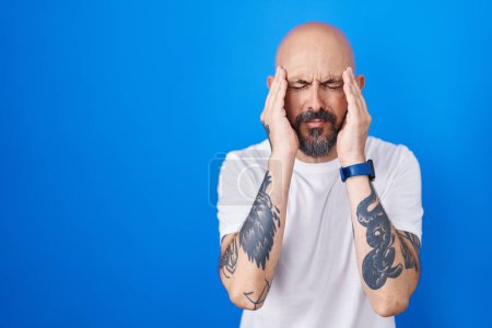 Photo for Hispanic man with tattoos standing over blue background with hand on head, headache because stress. suffering migraine. - Royalty Free Image
