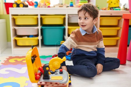 Photo for Adorable hispanic boy playing with technician tools toy sitting on floor at kindergarten - Royalty Free Image