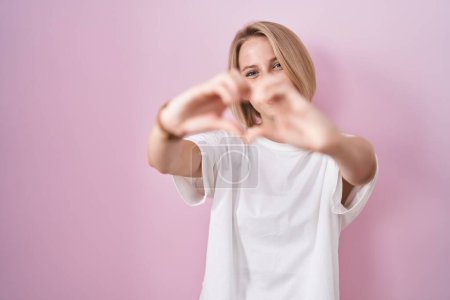 Photo for Young caucasian woman standing over pink background smiling in love doing heart symbol shape with hands. romantic concept. - Royalty Free Image