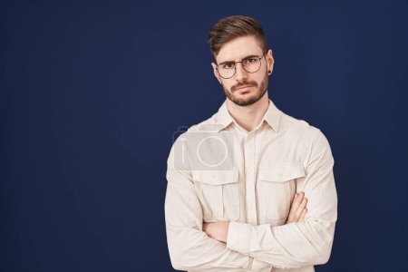 Photo for Hispanic man with beard standing over blue background skeptic and nervous, disapproving expression on face with crossed arms. negative person. - Royalty Free Image