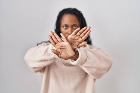 Foto de Mujer africana de pie sobre fondo blanco expresión rechazo cruzando brazos y palmas haciendo signo negativo, cara enojada - Imagen libre de derechos