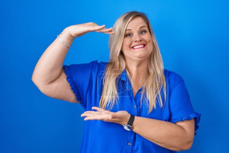 Photo for Caucasian plus size woman standing over blue background gesturing with hands showing big and large size sign, measure symbol. smiling looking at the camera. measuring concept. - Royalty Free Image