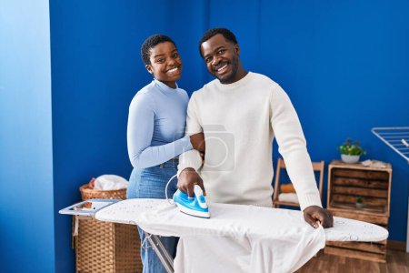 Téléchargez les photos : Homme et femme couple souriant vêtements de repassage confiants à la buanderie - en image libre de droit