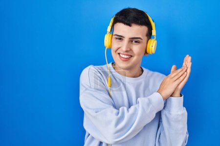 Téléchargez les photos : Non binary person listening to music using headphones clapping and applauding happy and joyful, smiling proud hands together - en image libre de droit