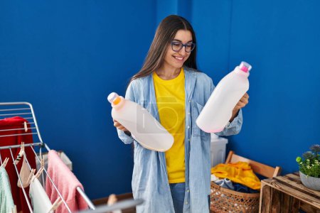 Téléchargez les photos : Young hispanic woman smiling confident holding detergent bottles at laundry room - en image libre de droit