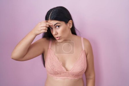 Photo for Young hispanic woman wearing pink bra pointing unhappy to pimple on forehead, ugly infection of blackhead. acne and skin problem - Royalty Free Image