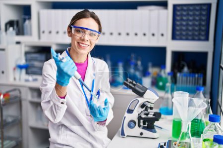 Photo for Young beautiful hispanic woman scientist smiling confident pouring liquid on sample at laboratory - Royalty Free Image