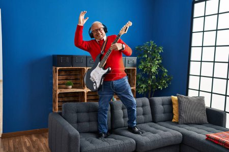 Foto de Hombre mayor tocando la guitarra eléctrica de pie en el sofá en casa - Imagen libre de derechos