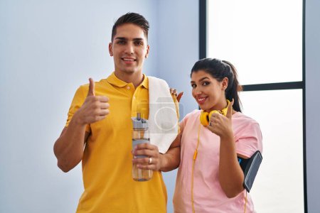Photo for Young couple wearing sportswear and headphones smiling happy and positive, thumb up doing excellent and approval sign - Royalty Free Image