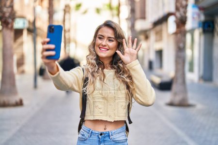 Foto de Joven turista sonriendo confiada teniendo videollamada en la calle - Imagen libre de derechos