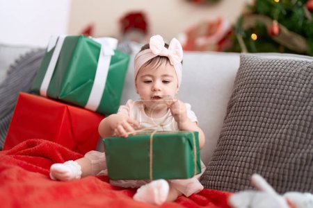 Téléchargez les photos : Adorable tout-petit ouverture cadeau de Noël assis sur le canapé à la maison - en image libre de droit