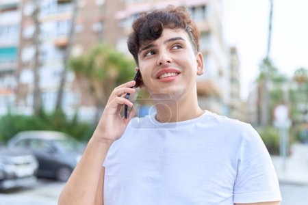 Foto de Hombre no binario sonriendo confiado hablando en smartphone en la calle - Imagen libre de derechos