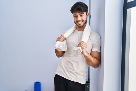 Téléchargez les photos : Jeune homme hispanique souriant et confiant portant une serviette au centre sportif - en image libre de droit