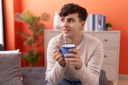 Téléchargez les photos : Non binary man drinking coffee sitting on sofa at home - en image libre de droit