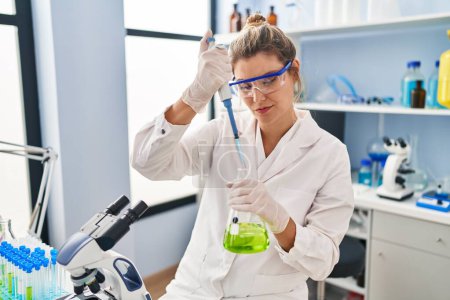 Photo for Young blonde woman wearing scientist uniform using pipette at laboratory - Royalty Free Image