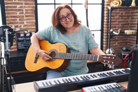 Téléchargez les photos : Senior musicien souriant confiant jouer de la guitare classique au studio de musique - en image libre de droit