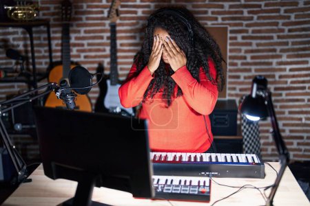 Téléchargez les photos : Femme hispanique de taille plus jouant du piano dans un studio de musique avec une expression triste couvrant le visage avec les mains tout en pleurant. concept de dépression. - en image libre de droit