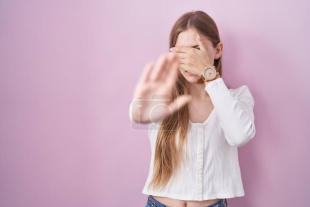 Foto de Young caucasian woman standing over pink background covering eyes with hands and doing stop gesture with sad and fear expression. embarrassed and negative concept. - Imagen libre de derechos