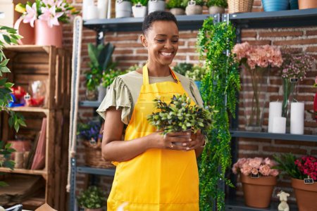 Foto de Mujer afroamericana florista sosteniendo planta en floristería - Imagen libre de derechos