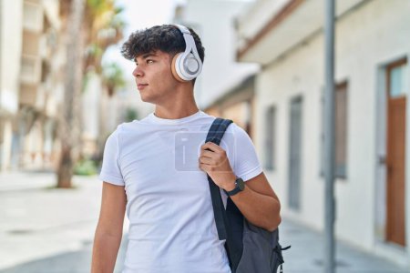 Foto de Joven estudiante adolescente hispano escuchando música con expresión relajada en la calle - Imagen libre de derechos