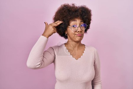 Foto de Joven mujer afroamericana de pie sobre fondo rosa disparando y matándose señalando la mano y los dedos a la cabeza como arma, gesto suicida. - Imagen libre de derechos