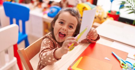 Téléchargez les photos : Adorable hispanic girl student smiling confident cutting paper at kindergarten - en image libre de droit