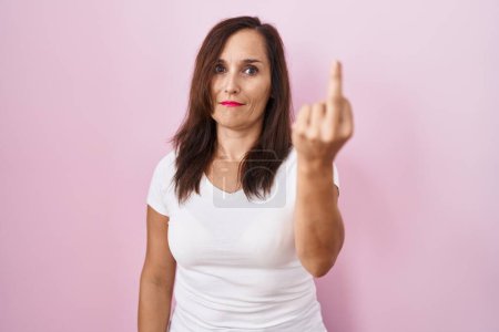 Foto de Middle age brunette woman standing over pink background showing middle finger, impolite and rude fuck off expression - Imagen libre de derechos