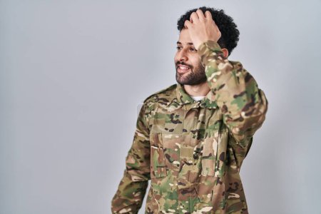 Téléchargez les photos : Arabe homme portant uniforme camouflage armée souriant confiant toucher les cheveux avec geste de la main vers le haut, posant attrayant et à la mode - en image libre de droit