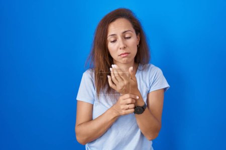 Foto de Brunette woman standing over blue background suffering pain on hands and fingers, arthritis inflammation - Imagen libre de derechos