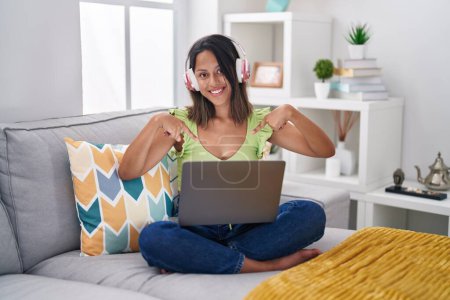 Téléchargez les photos : Jeune femme hispanique utilisant un ordinateur portable à la maison regardant confiant avec le sourire sur le visage, se montrant du doigt fier et heureux. - en image libre de droit