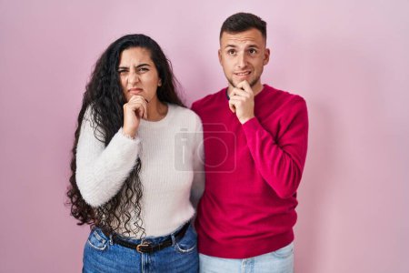 Téléchargez les photos : Jeune couple hispanique debout sur fond rose pensant inquiet d'une question, inquiet et nerveux avec la main sur le menton - en image libre de droit