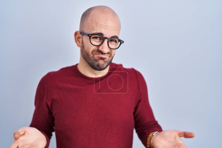 Téléchargez les photos : Young bald man with beard standing over white background wearing glasses clueless and confused with open arms, no idea concept. - en image libre de droit