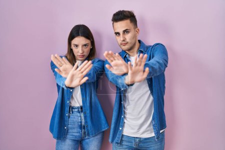 Téléchargez les photos : Jeune couple hispanique debout sur fond rose expression de rejet croisement des bras et des paumes faisant signe négatif, visage en colère - en image libre de droit